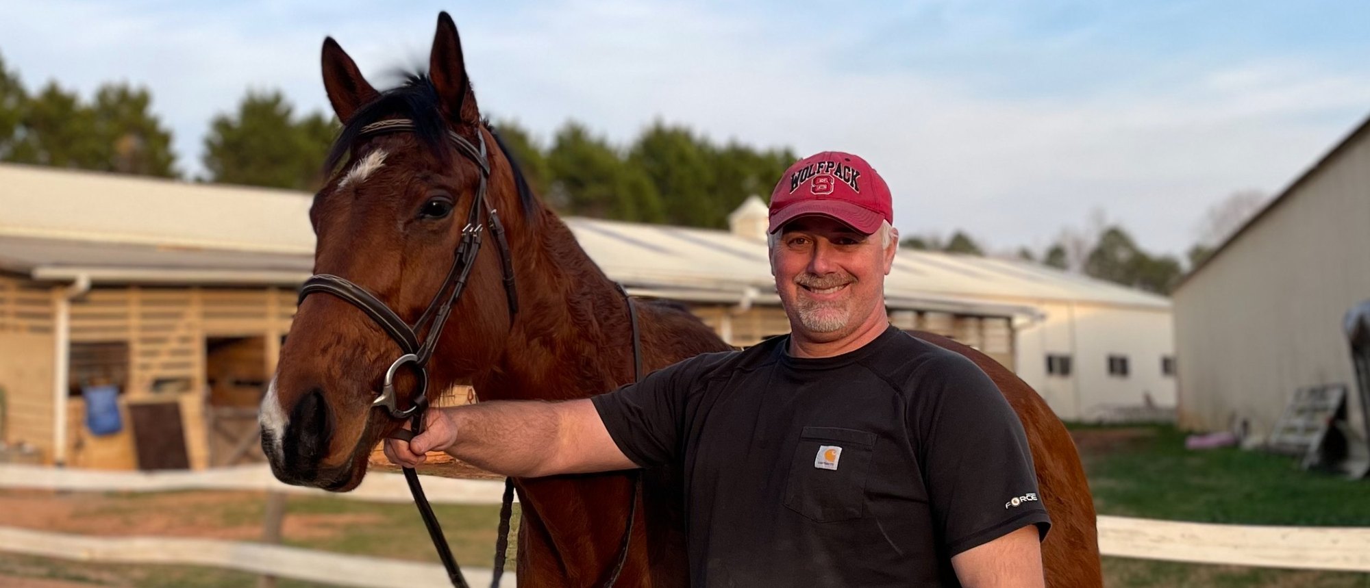 Dennis with a bay horse outside the stable at sunset