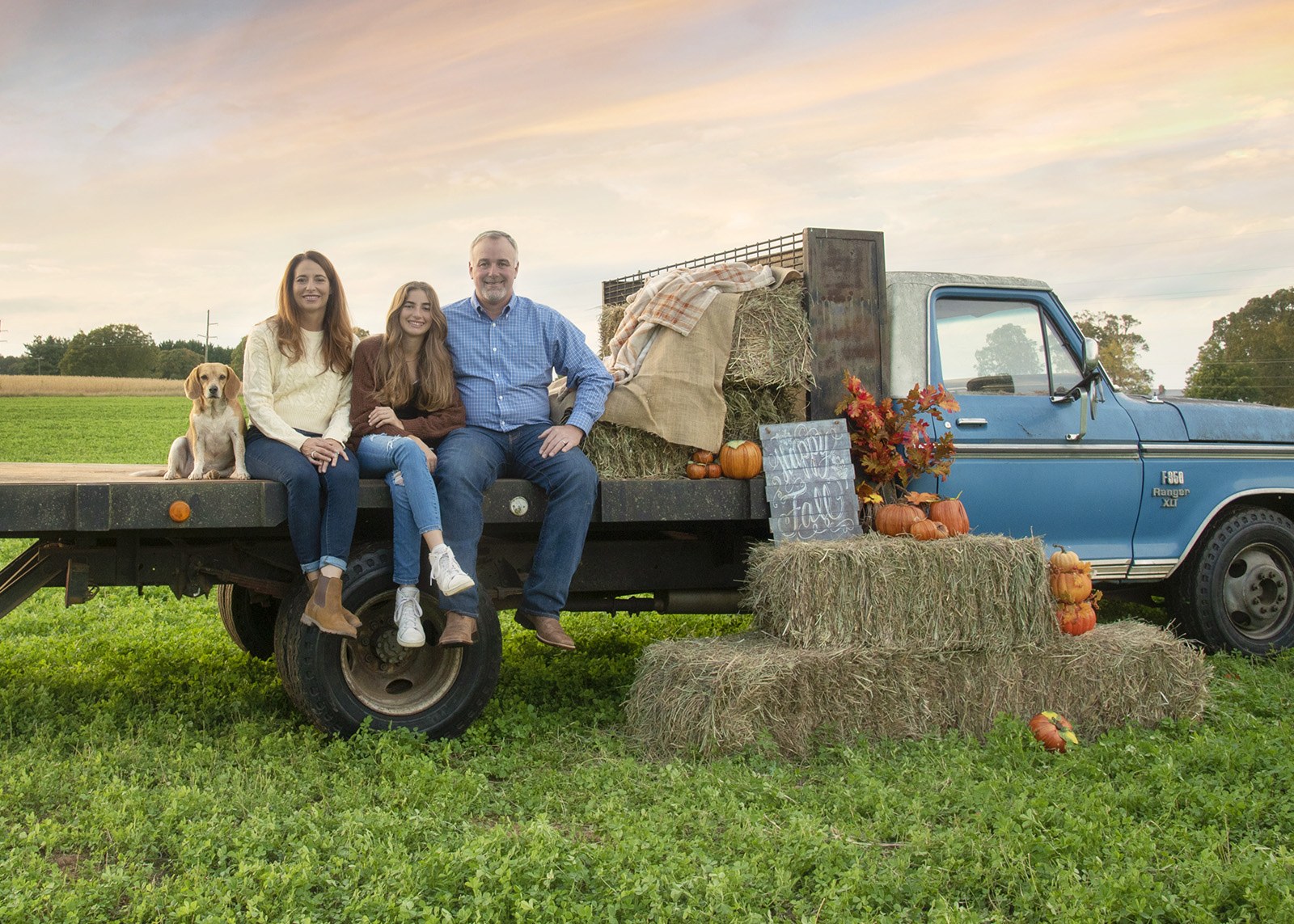 Family on the vintage Ford F-350 with hay and pumpkins at sunset
