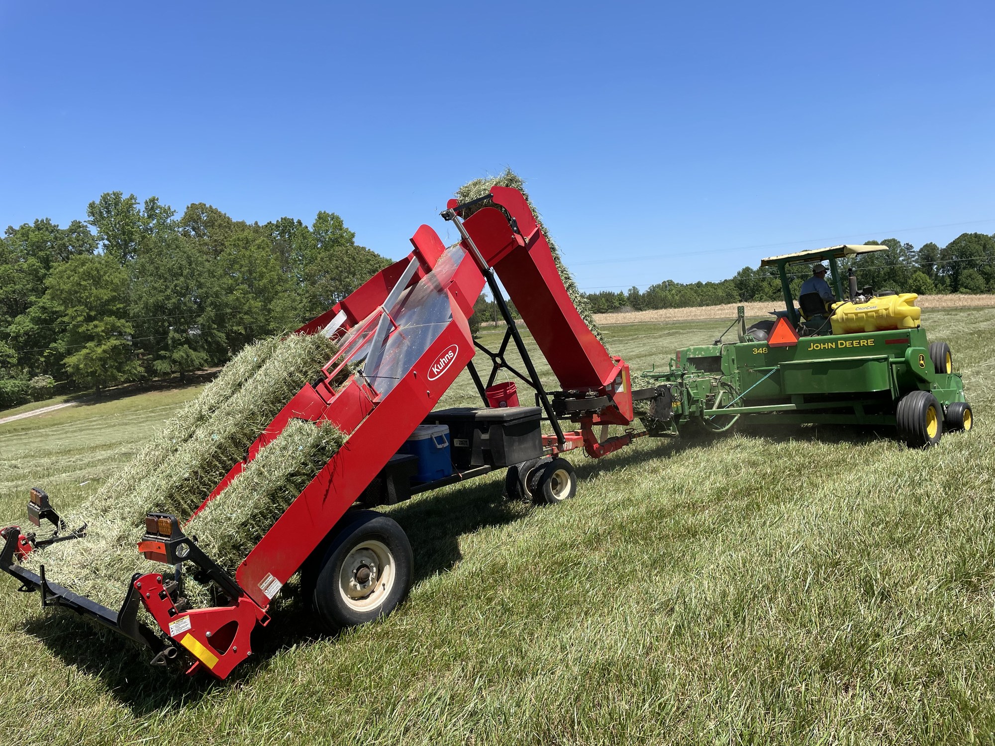 Kuhns bale accumulator with John Deere baler under a brilliant blue sky